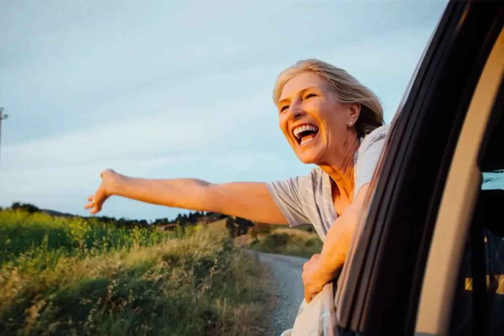 Mulher com parte do corpo para fora da janela de um carro e muito feliz
