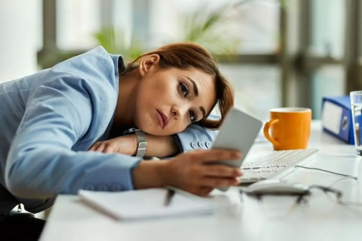Procrastinação Por Que Acontece e Como Vencer o Hábito de Adiar Tarefas - Mulher mexendo no celular ao invés de trabalhar