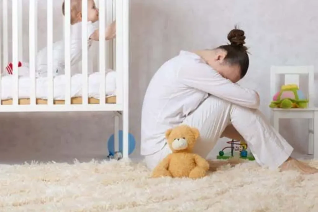 Bebê no berço e mulher triste sentada no chão